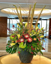 Arrangement floral contemporain avec protéas, lys, baies rouges et feuilles de monstera — création pour un hall d’entreprise par McKenna Florist à Montréal.